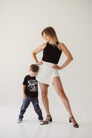 In a bright and stylish studio environment, a fashionable mother stands confidently beside her son, showcasing their modern style and the strong family connection they shareの写真素材
