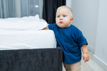 In a cozy bedroom filled with delightful decor, a curious toddler in a blue shirt joyfully explores vibrant toys next to a comfy bed, radiating innocence and joyの写真素材