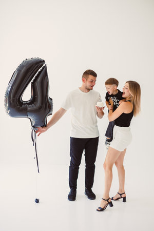 A joyful family moment unfolds as a loving couple spends time with their adorable child, celebrating a milestone with a large black number 4 balloon in a bright studioの写真素材