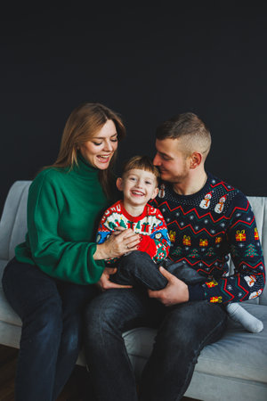 A joyful child and loving parents, in colorful holiday sweaters, share radiant smiles in a cozy indoor setting, exuding warmth and happiness during the festive seasonの写真素材