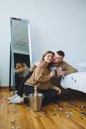 A joyful couple celebrates a special occasion at home, raising champagne glasses while colorful confetti fills the air, creating a festive atmosphere of love and laughterの写真素材