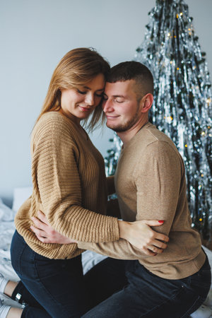 A cozy, romantic moment shared by a couple in matching sweaters, surrounded by a beautifully decorated Christmas tree, embodying love and joy during the holiday season.の写真素材