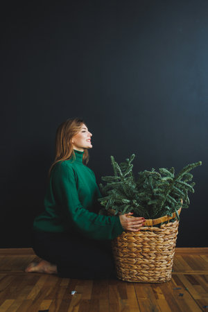 A woman in a cozy green sweater joyfully engages with a beautifully arranged basket of plants, creating a calm and inviting atmosphere in a stylish indoor spaceの写真素材
