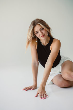 A fashionable young woman with beautiful wavy hair strikes a pose in a chic black top paired with a flowing white skirt, radiating an air of elegance, style, and confidenceの写真素材