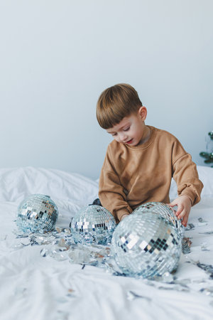 A lively child joyfully plays with sparkling disco balls on a cozy bed, creating a colorful atmosphere perfect for festive gatherings, making each moment specialの写真素材