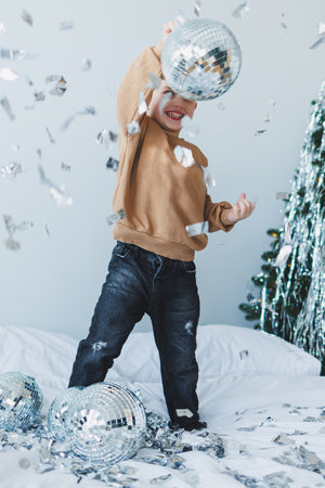 A joyful child twirls with a sparkling disco ball as colorful confetti showers down, capturing the essence of celebration and excitement in a festive atmosphereの写真素材