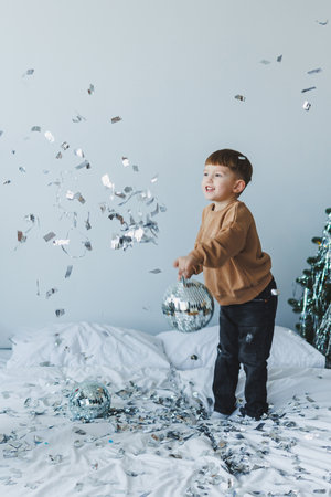 A delighted child plays with a shiny disco ball and colorful confetti, creating a festive atmosphere indoors, perfect for joyful celebrations and memorable family momentsの写真素材