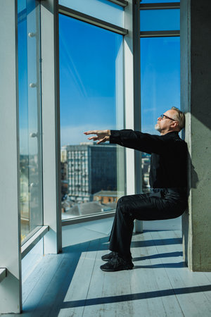 A person meditates peacefully against a glass wall, captivated by the city skyline and natural...
