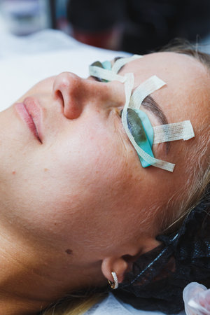 A serene woman receiving a lash extension treatment, with protective pads securing her lower lashes, showcasing the beauty and care involved in cosmetic procedures.の写真素材