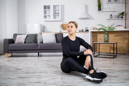 A passionate female athlete stretches in a modern living room, inspiring others to embrace wellness and fitness in a cozy, positive atmosphere promoting healthy habitsの写真素材