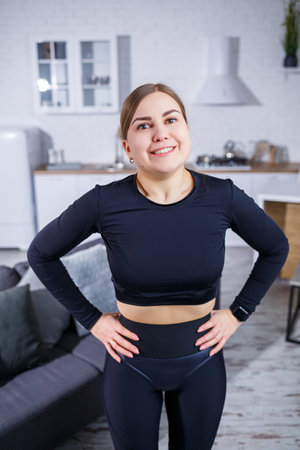 A cheerful young woman in stylish activewear stands confidently in her beautifully designed home, ready to start her invigorating workout and embodying a healthy lifestyleの写真素材
