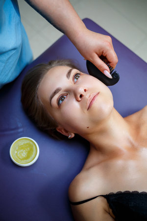 A young woman is lying on a couch and she is having a face massage, skin care, prevention of wrinkles on the face, skin improvement. Beauty procedures for womenの写真素材