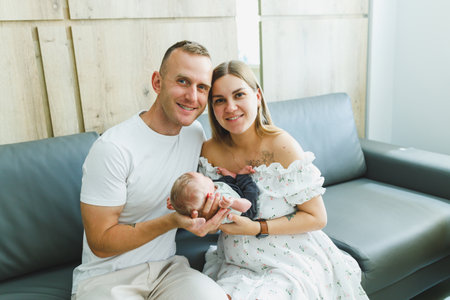 In a cozy room filled with soft light, a joyful couple holds their newborn baby, capturing a heartfelt moment symbolizing their love and hopeful family beginningsの写真素材