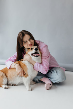A woman dressed in a pink shirt hugs her smiling corgi in a cozy setting, showcasing the bond between pets and their ownersの写真素材