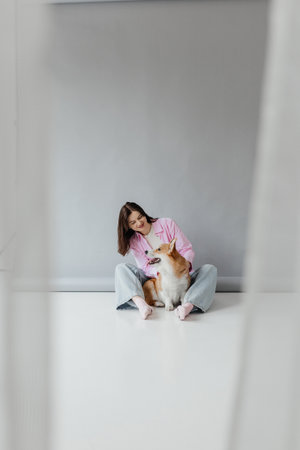 A young woman in loungewear shares a joyful moment with her adorable corgi in a serene, modern space that promotes relaxation and highlights their companionshipの写真素材