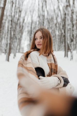 A young woman snugly wrapped in a warm blanket enjoys a beautiful and serene winter wonderland, surrounded on all sides by majestic, snowcovered trees under a clear skyの写真素材