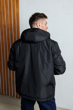 A man dressed in a stylish black puffer jacket featuring a cozy hood, photographed from the back, highlighting its contemporary design and adaptability for numerous occasionsの写真素材