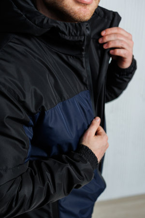 A stylish and fashionable young man dressed in a contemporary black and navy jacket is striking a...