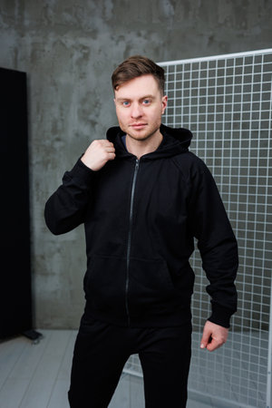 A trendy young man confidently sports a stylish black hoodie while striking an impressive pose in a modern contemporary studio setting, ideal for lifestyle and fashion themesの写真素材