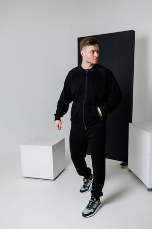 A confident young man walks gracefully in a sleek black tracksuit, showcasing modern athletic style against a minimalist studio backdrop, adding elegance to the sceneの写真素材