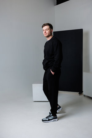 In a minimalist studio, a fashionable young man dons sleek black attire, standing confidently to showcase his modern streetwear style, which radiates a refined sense of eleganceの写真素材