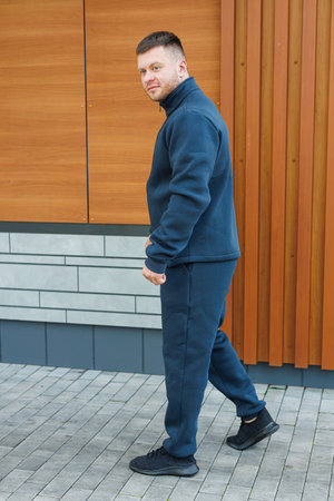 A confident man in a sleek dark fleece outfit stands on a modern urban street, showcasing his stylish and comfortable athletic wear for casual outings with friendsの写真素材