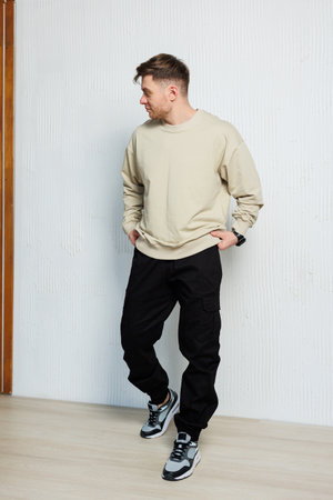 A male model confidently showcases contemporary streetwear with a cozy beige sweater and sleek black jogger pants, perfect for casual outings and vibrant urban scenesの写真素材