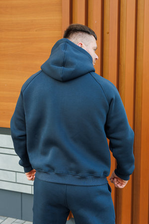 A stylish young man, dressed in a trendy navy blue hoodie, stands confidently against a rustic wooden wall, perfectly showcasing a casual yet fashionable look ideal for urban lifeの写真素材