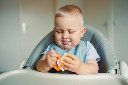 Smiling boy sitting in a high chair, eating yogurt in the kitchen. Healthy food for children....