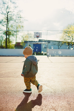 Cheerful 2 year old boy playing outside in summer. Toddler boy running outside and playing with bubbles.の写真素材
