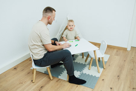 Dad teaches his 1.6 year old son to sculpt from plasticine. The toddler boy sits at the children's table with his dad and plays entertaining games. The child sculpts figures from plasticineの写真素材