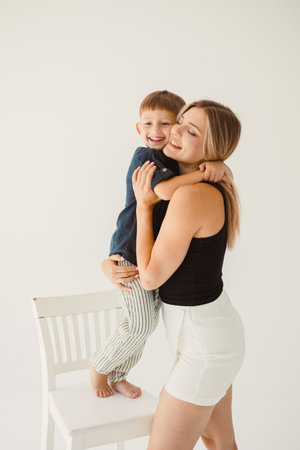 Cute mother and baby boy hugging while sitting on white background. Happy mother and baby son waiting for dad to return from work. Fun games of mother and son.の写真素材
