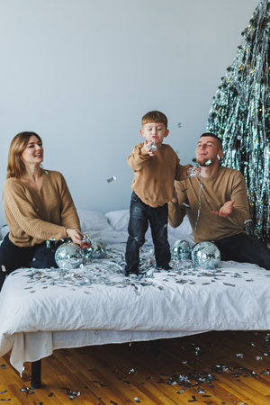 In a cozy home adorned with sparkly decorations, a child joyfully throws colorful confetti, creating a lively atmosphere of laughter during a cherished family celebrationの写真素材