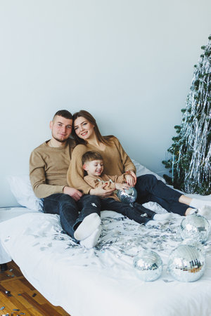 In a cozy bedroom, a happy family is gathered on their comfortable bed, surrounded by Christmas decorations, sharing joy and laughter during the festive seasonの写真素材