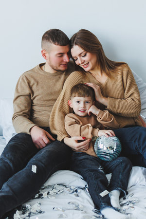 A loving family of three enjoys a truly joyful time together on their cozy bed, sharing bright smiles and hearty laughter while playing with a sparkling, colorful ballの写真素材