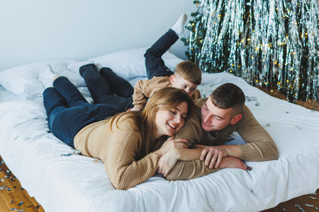 A loving couple snuggles warmly with their adorable child on a cozy bed, joyfully celebrating their precious love during the magical and festive winter holiday season togetherの写真素材