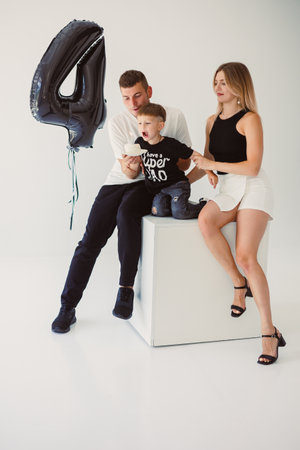 A joyful family moment capturing a child's 4th birthday celebration, featuring playful interactions with parents and a stylish balloon backdrop in a minimalist studio.の写真素材
