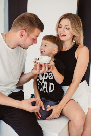 A delightful family scene featuring parents joyfully sharing a sweet treat with their playful child, capturing moments of love and togetherness in a stylish setting.の写真素材