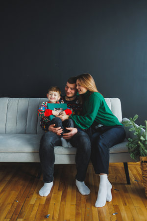 A happy family sits together on a couch, wearing festive sweaters. They share a warm embrace, capturing the essence of love and togetherness during the holidays.の写真素材