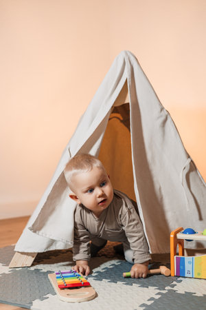 A cheerful toddler crawls out of a colorful play tent, joyfully diving into a large pile of vibrant toys in a stylish playroom for endless exploration and creativityの写真素材
