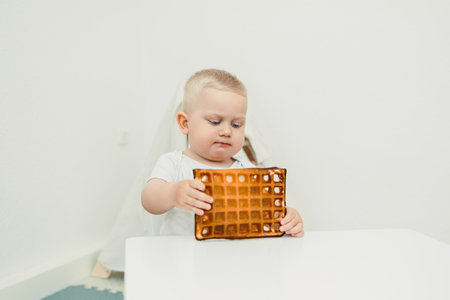 A young child, full of wonder and curiosity, intently studies a perfectly cooked waffle, showcasing...