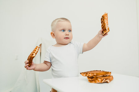 In a lovely, modern kitchen setting, a cute baby joyfully holds a delicious stack of waffles, delighting in a moment of exploration and pure joy, perfect for family contentの写真素材