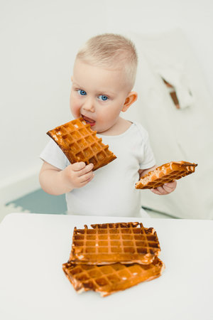 A cheerful baby bites into a crispy waffle, surrounded by tasty treats, capturing the joy of sweet indulgence and cherished family moments filled with love and laughterの写真素材