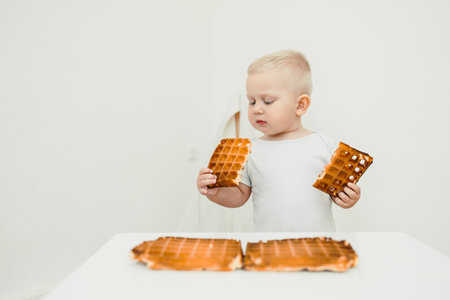 In a clean and bright environment, a delightful toddler intently examines two pieces of delicious waffle, showcasing both their natural curiosity and the pure joy of discoveryの写真素材