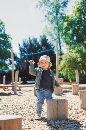 A joyful toddler explores a natureinspired playground, confidently standing on a sturdy wooden stump while enjoying the warm sunshine on this lovely day outdoorsの写真素材