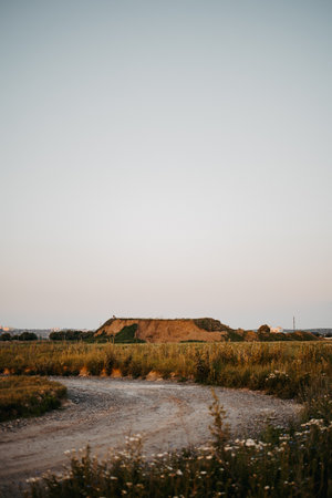 A tranquil rural landscape features a winding gravel path leading to soft hills under a serene evening sky, showcasing natures stunning beauty and deep serenityの写真素材