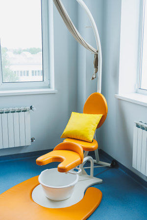 This ergonomic dental chair features a vibrant orange finish and a soft yellow pillow, creating a comfortable and welcoming environment with plenty of natural lightの写真素材