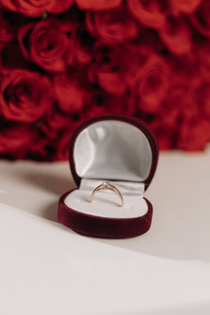 A stunning gold ring in a luxurious red velvet box, surrounded by vibrant roses, ideal for...