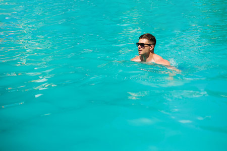 A man is enjoying a delightful and refreshing swim in a stunning turquoise pool, which beautifully...