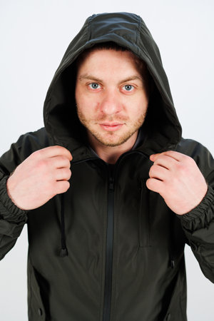 A young man with a determined and focused expression is adjusting his stylish hooded jacket, confidently exuding both style and poise within a minimalistic settingの写真素材